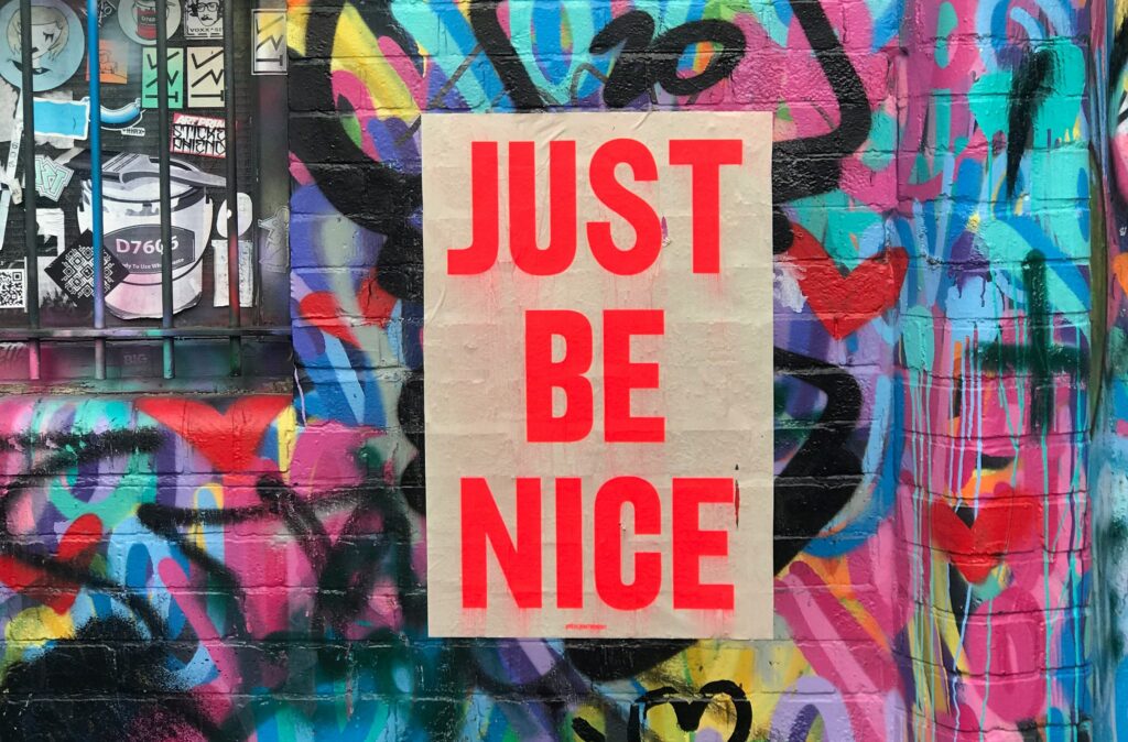 Texto "JUST BE NICE" pintado en una pared colorida con tonos vibrantes