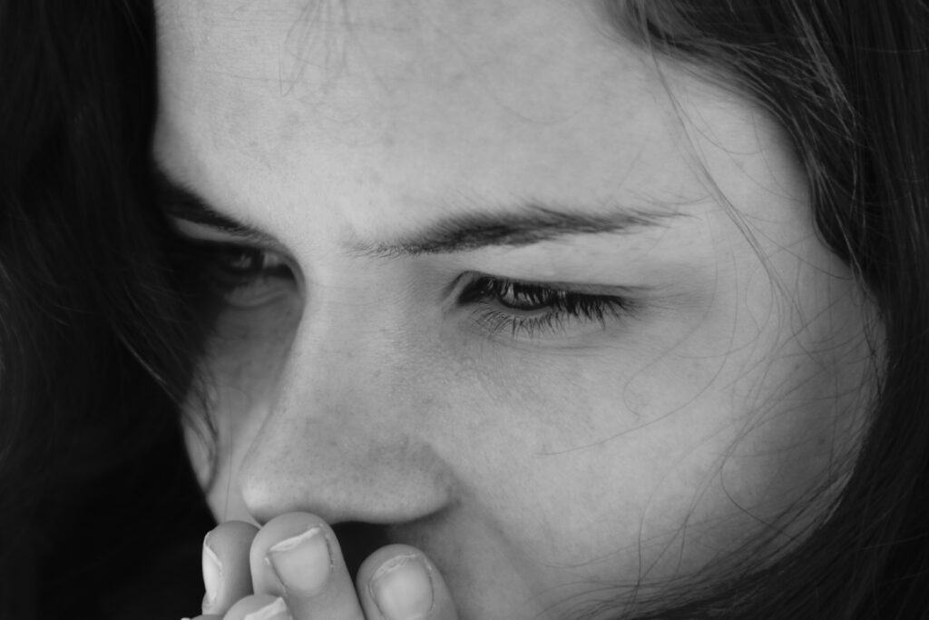 Mujer pensativa en primer plano, con las manos sobre la boca y la mirada perdida en el vacío.
