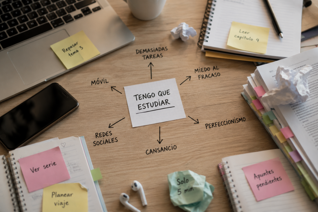 Escritorio de estudio con apuntes, portátil, móvil y notas adhesivas que representan visualmente las causas de la procrastinación académica.