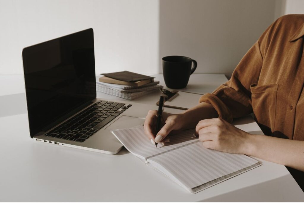 Persona escribiendo en un cuaderno mientras deja el ordenador a un lado, simbolizando reflexión consciente y acción para equilibrar la relación con la tecnología.